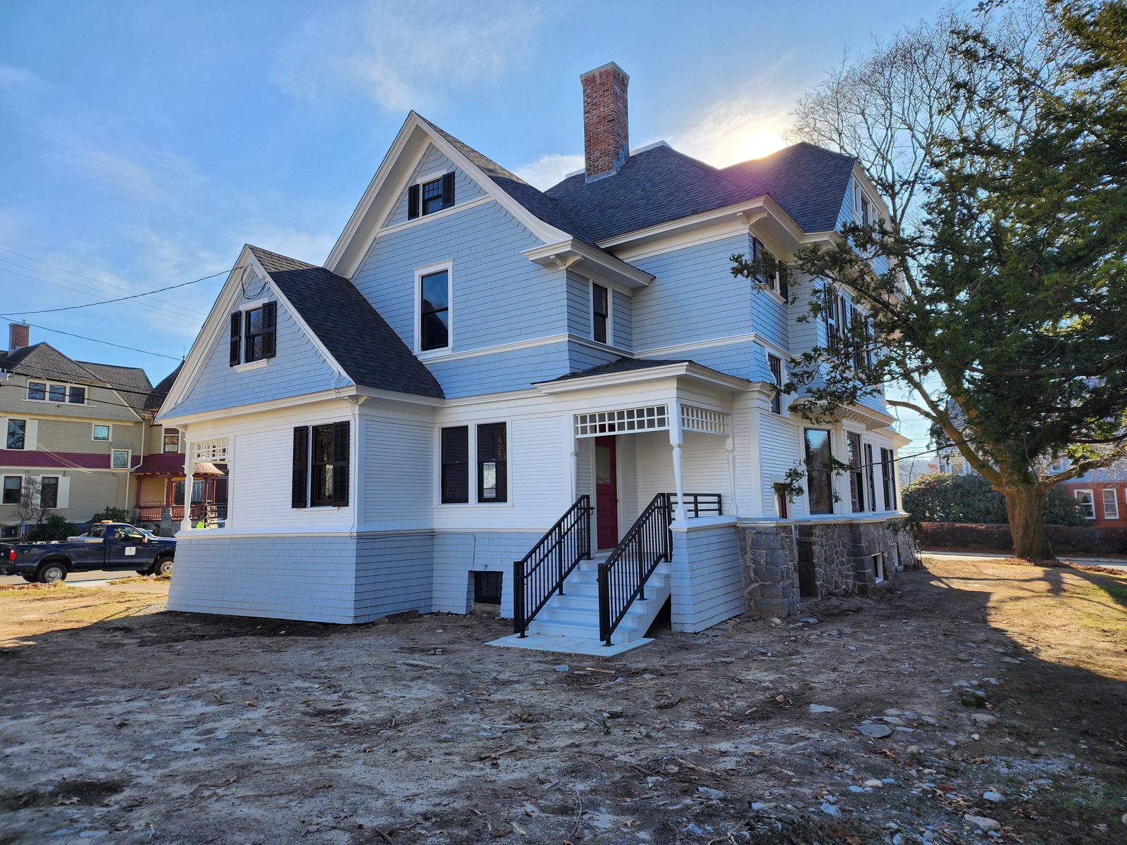 Rear elevation after restoration: white clapboard gables, rebuilt brick chimney, and a new rear entry with granite steps and black steel railings above the repointed stone foundation
