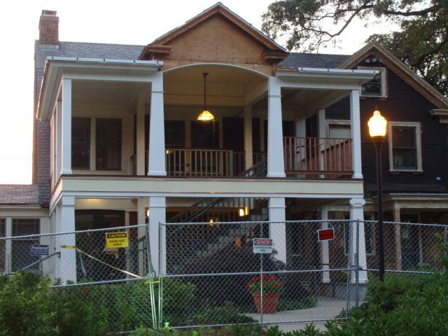Two-story porch under restoration behind construction fencing