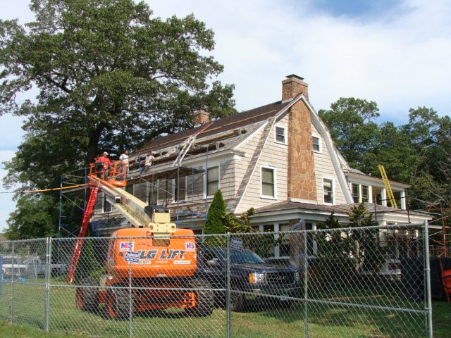 Boom lift at the roof of a shingled campus house during slate roof work