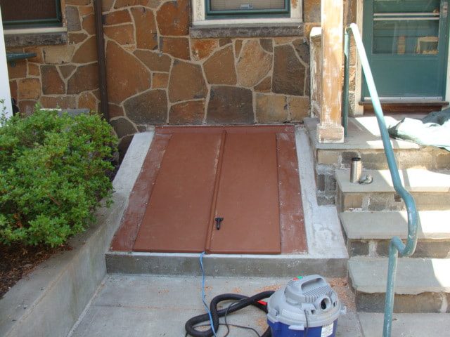New steel bulkhead cellar door set in concrete beside the stone foundation