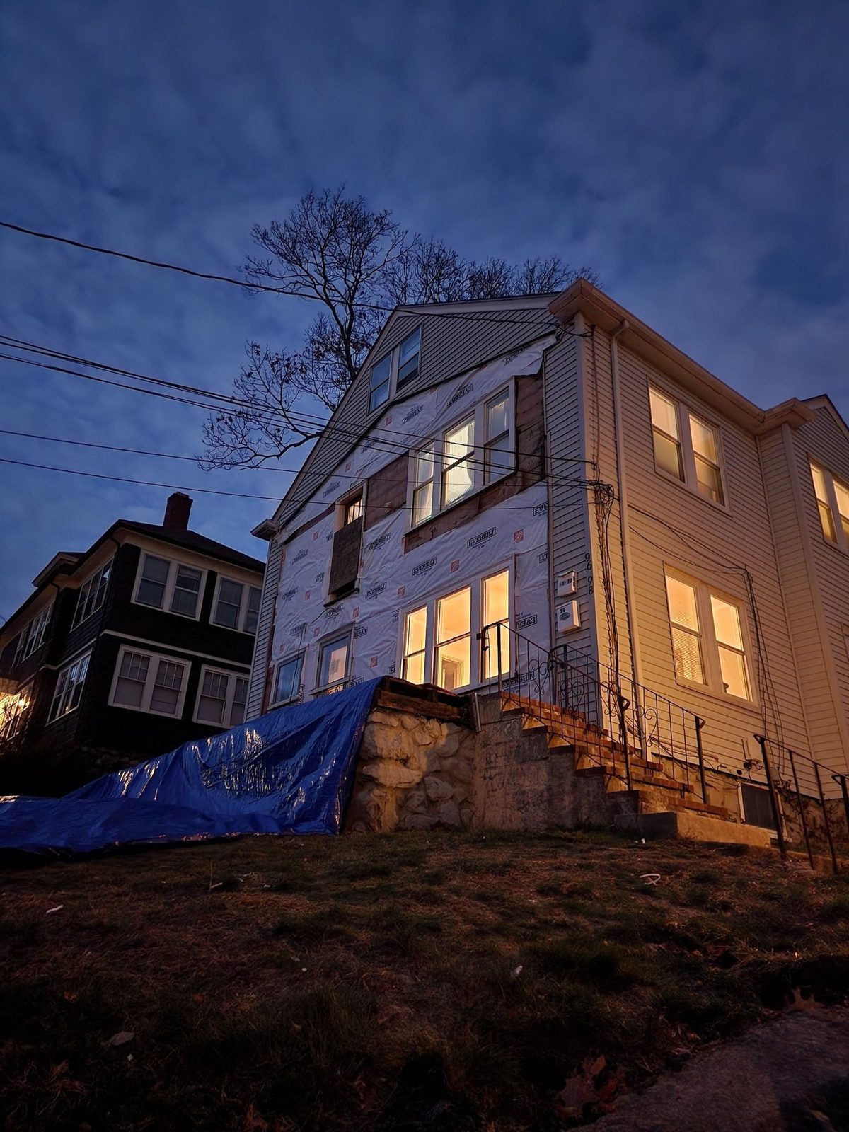 The addition at dusk in house wrap, with new windows lit from inside