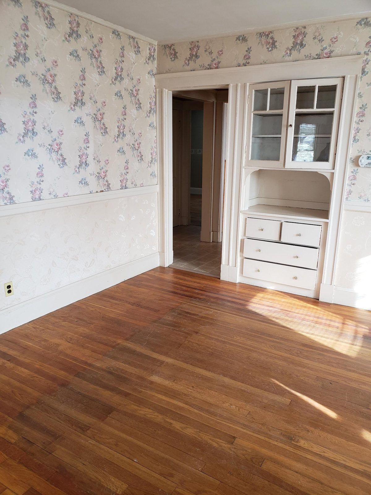 Dining room before the work, with floral wallpaper, a built-in china cabinet and worn hardwood floor